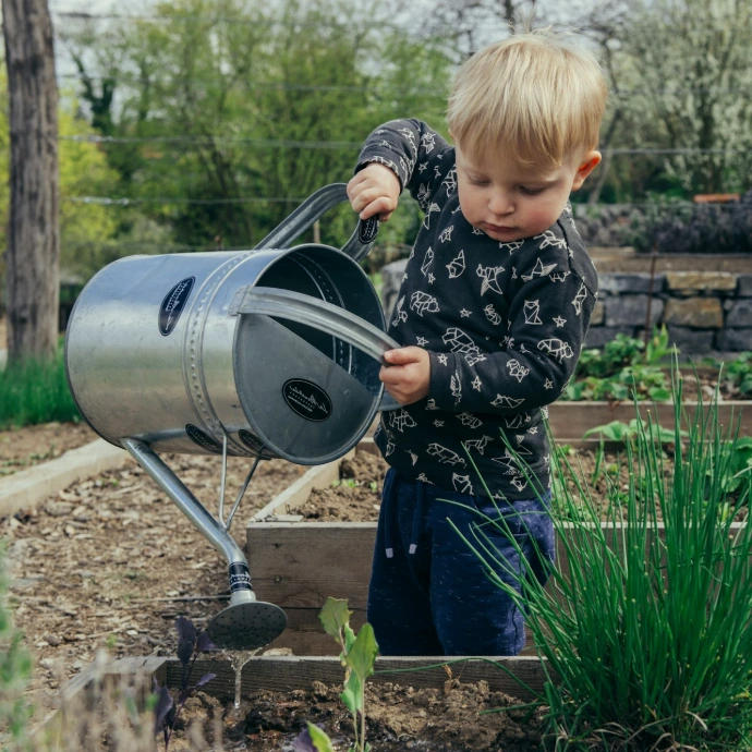 boy in black and white long sleeve shirt standing beside gray metal watering can during daytime